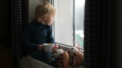 Sticker - Toddler child, sitting on the window, watching the snow falling, reading little book