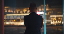 Back View Of Successful Young Businessman In Suit Is Looking Out Of Panoramic Window.