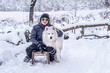 © alonaphoto - Focus on the boy. Happy boy teen playing sledding with a samoyed dog outdoors in winter. Friendship of the child and dog. Isolation in quarantine of coronavirus, covid19. Winter activities in the snow