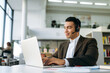 © Kateryna - Smiling manager at the workplace, uses laptop. Handsome male hispanic employee works on project or new startup, sit at the desk in office, wearing headset, communicate with colleagues