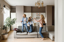 Happy Three Generations. Cheerful Caucasian Mom Daughter And Modern Grandmother Are Having Fun At Home Together, They Are Dancing, Jumping On The Sofa, Fooling Around And Laughing
