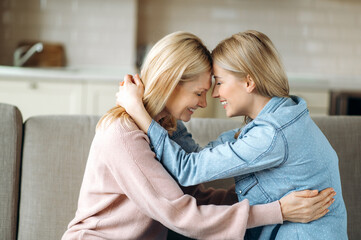 sensual photo of aged blonde caucasian mother and her young adult happy daughter, are sitting at hom