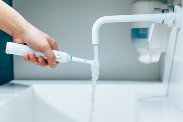 Wall Mural - hand holding a toothbrush under flowing water from faucet in a bathroom