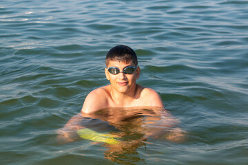 Teenager in goggles swims in the sea with big splashes. Cute boy enjoys swimming in the ocean.  Holidays, vacation with kids