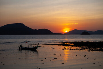 Sticker - A silhouette of a fisherman and a long tail boat made of wood Floating on the beach By the sea, at sunset The sky is a beautiful orange color, the seaside in Phuket Thailand.