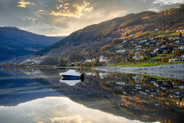 Wall Mural - A boat floats in a lake in Voss, Norway, the still water looks like a mirror, reflecting the house on the hill with the trees in the autumn in the evening, the atmosphere is calm and relaxed.