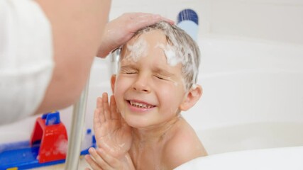 Wall Mural - Closeup slow motion of mother holding shower head and washing head of her little son sitting in bath. Concept of child hygiene and health care at home. Family having time together and playing at home