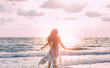 Silhouette of beautiful young happy woman tourist walks runs by coastline. girl admires beauty bright divine sun light sea sunset. Blue pink clouds sky. Fluttering long hair back view. silk dress fly