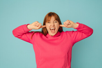 Wall Mural - Closing ears. Caucasian woman's portrait on blue studio background with copyspace. Beautiful female model in pink sweatshirt. Concept of human emotions, facial expression, sales, ad, fashion.