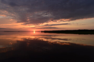 Wall Mural - Sky in the brightly lit twilight of a sunset over picturesque  lake water with  reflection clouds and  sunbeam on the horizon over the water surface