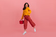 © Look! - Perky girl in stylish glasses stares into camera in amazement, walking on pink background. Brunette in culottes and orange blouse posing with red handbag