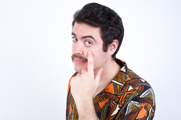 Young caucasian man wearing generic pattern printed shirt against yellow wall Pointing to the eye watching you gesture, suspicious expression.