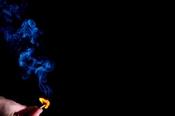 Blue curly smoke from a lit match in a holding hand isolated on a black background. Abstract mystical smoke for your photos. Smoke from a match