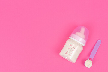 Powder in spoon near baby bottle on pink background