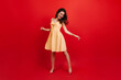 Full-length shot of active woman dancing on red background. Lady in sundress and heels having fun