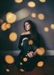 © Cavan Images - Pensive pretty woman sitting on floor with light bokeh surrounding her
