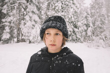 Young Boy In A Beanie Looks Away While Snowflakes Fall Around Him.