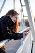 © Cavan Images - young adult woman laughing in a footbridge with her phone