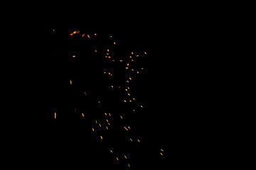 Particles of burning embers fly and glow isolated in the night sky. Blurred bright sparks on black background, yellow hot blurred lights on dark background.