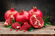 Several ripe pomegranate fruits and an open pomegranate with pomegranate leaves on a wooden old cutting board, side view, dark background.