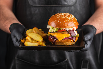 Wall Mural - Grilled hamburger with meat cutlet and French fries in hands. Fast food concept. Homemade burger. Fried potatoes and cheeseburger.