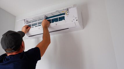 Maintenance of the air conditioner. A technician is cleaning the filter. View of the hands from the back.