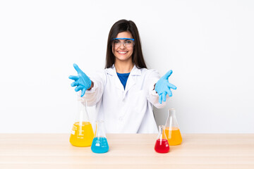 Young scientific woman in a table presenting and inviting to come with hand