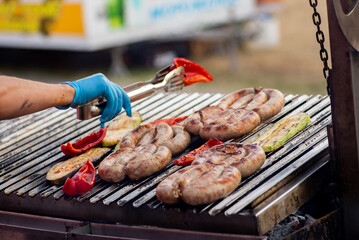 Wall Mural - Cook turns over the grilled sausage and vegetables. Street food. BBQ picnic