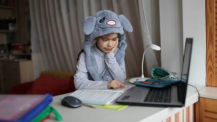 Wall Mural - Distant education, online class meeting, reading. Pretty schoolgirl wearing funny rabbit hat with ears to amuse classmates during lesson at home, social distance during quarantine, self-isolation