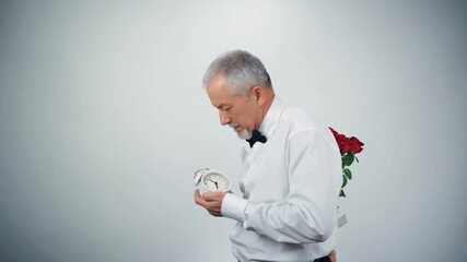 Wall Mural - Funny grandfather with a beard in fashionable clothes with a bouquet of flowers and a watch in his hands sneaks on a date.