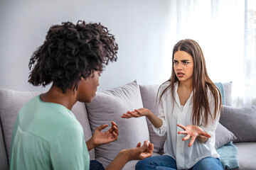 Two female friends sitting on sofa and arguing with each other. Friendship, quarrel, female disagreement, copy space. Two female friends sitting on sofa and arguing with each other.