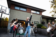 Teenage Girl Friends Practicing As Rock Band In Driveway Of House