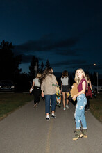 Portrait Teenage Girl With Skateboard On Path With Friends At Night