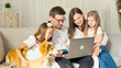 © alex_marina - A Happy Family Uses a Laptop for Online Shopping, Sitting on the Couch at Home. Buying by the Internet. A Familly Sitting With a Cute Dog on the Couch at Home. Purchase Confirmation by the Internet