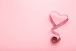 © fotoduets - Heart shape created from rolled out measure tape on light pink table background. Pastel color. Closeup. Empty place for text. Top down view.