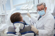 © mad_production - Senior male dentist wearing medical face mask, looking to the camera during dental appointment with patient