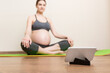 © sosiukin - Pregnant female holding smartphone while sitting on exercise yoga mat at home. Fitness or yoga training online at coronavirus time