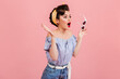 Shocked pinup girl holding sunglasses. Studio shot of emotional woman in vintage outfit isolated on pink background.