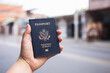 Human hand holding a blue American passport in front of a blurry background