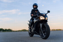 Attractive Girl In Black Leather Jacket, Pants And Helmet On Outdoors Parking Rides On Stylish Sports Motorcycle At Sunset.