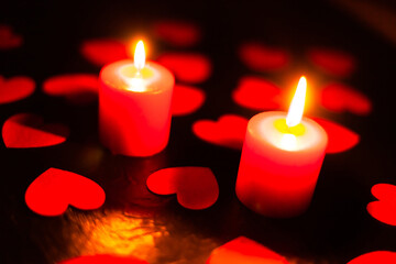 two red burning candles on a black textured background, around lie red hearts with blurry background, used as a background or texture, soft focus