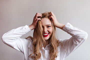 Wall Mural - Magnificent young girl touching blonde hair with smile. Studio shot of stylish female model in shirt.