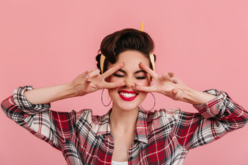 Sticker - Cheerful pinup girl posing with eyes closed and laughing. Studio shot of appealing young woman showing peace signs.