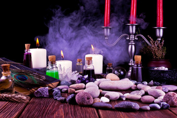 Magic potions, crystals, ancient book, stones, peacock feather and candles with smoke on a black background.