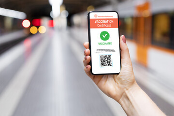 Person in train station holding mobile phone showing valid digital vaccination certificate