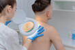 © salomonus_ - A dermatologist examines the skin on the body of a young man through a magnifying glass of a cosmetology lamp. Beauty treatments