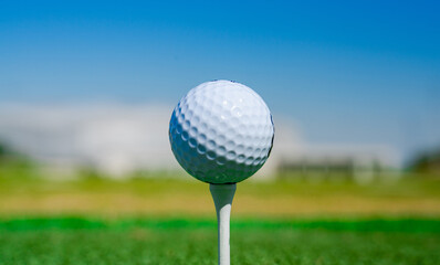 Wall Mural - Golf ball on tee on golf course over a blurred green field at the sunset. Golf ball on tee over a blurred green field.