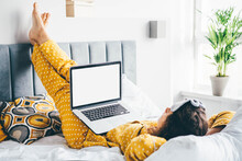 Woman in pajama at home on bed using laptop computer.