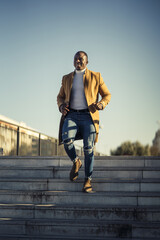 Wall Mural - Vertical shot of a stylish handsome smiling African male in a coat going down the stairs