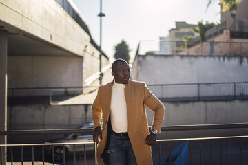 Wall Mural - Stylish handsome African male in a coat leaned on railing posing for the camera